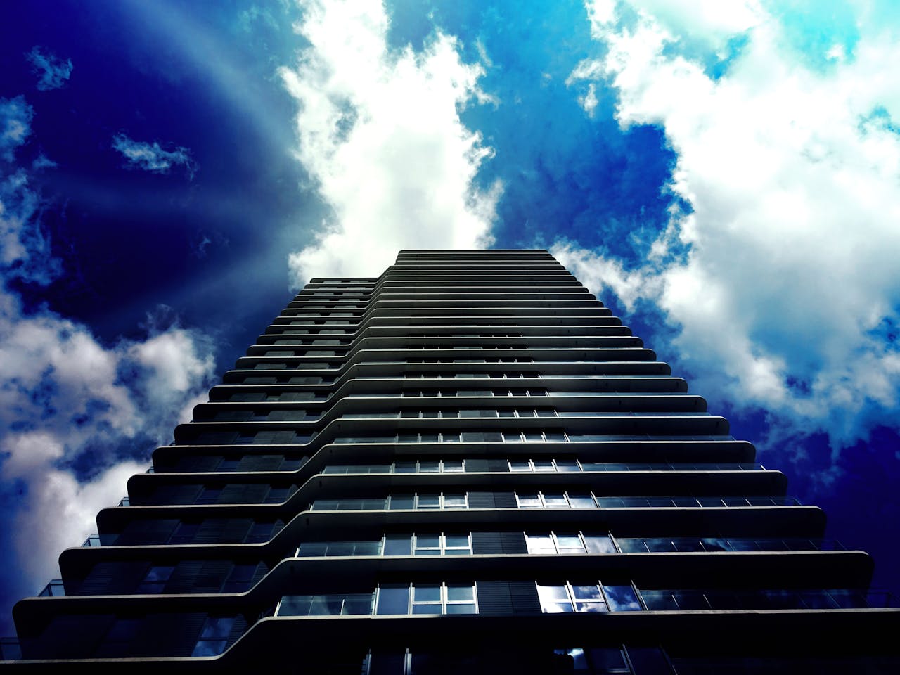 A low-angle view of a modern skyscraper with a vibrant blue sky and clouds in the background.